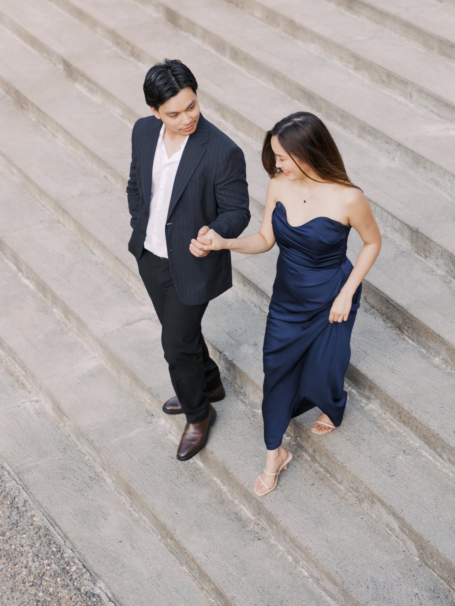 Engaged couple walking hand in hand down wide stone steps in Quebec City, seen from above