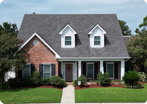 Two-story house with brick and white siding, gray roof, front porch, and green lawn with shrubs.