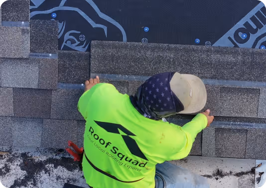 Worker wearing a bright green Roof Squad shirt installing asphalt shingles on a roof.