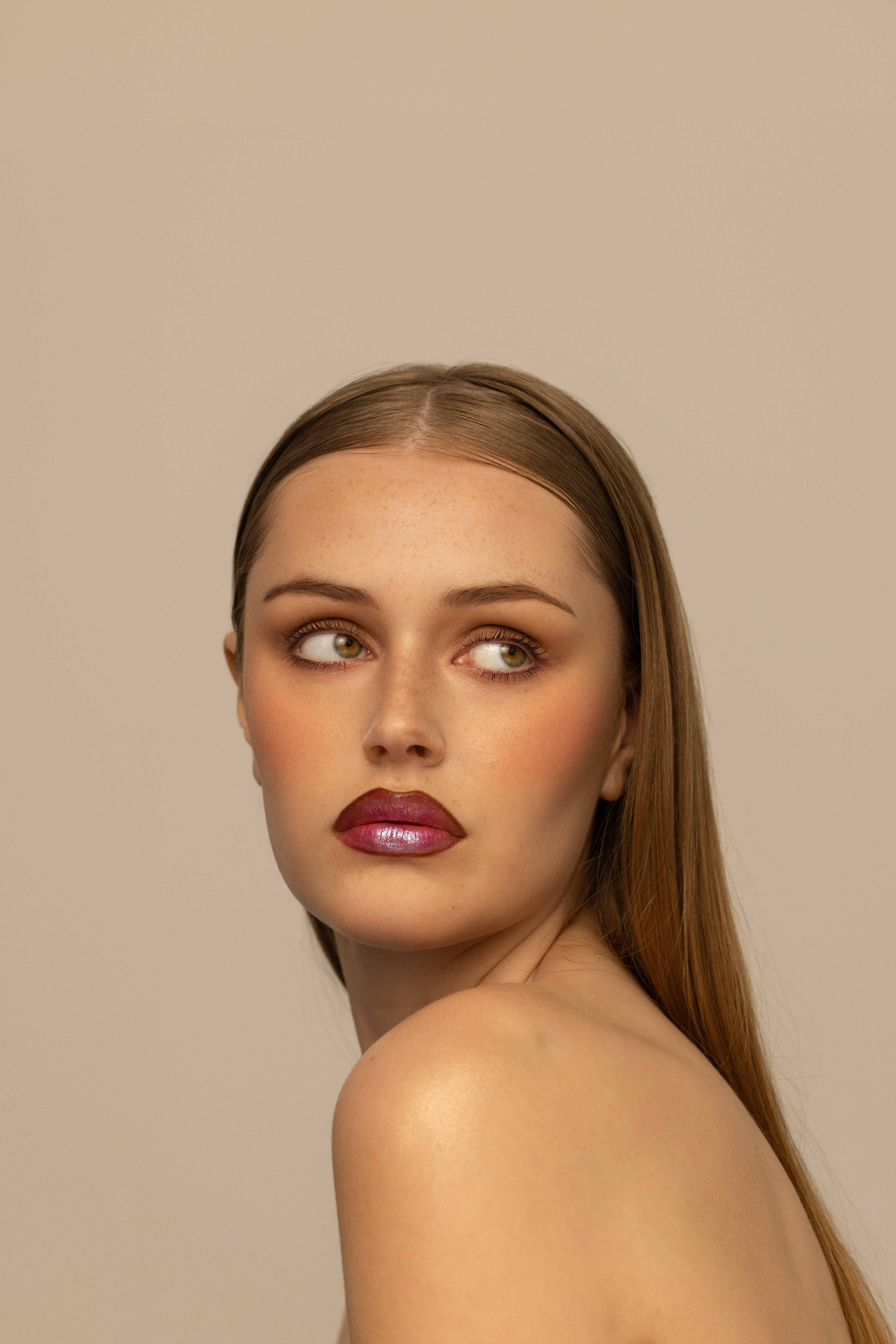 Artistic portrait of a woman with vibrant red crimped hair, soft pink blush, and a serene expression on a pastel gradient background – beauty photography by Kendra Storm Rae in Berlin.