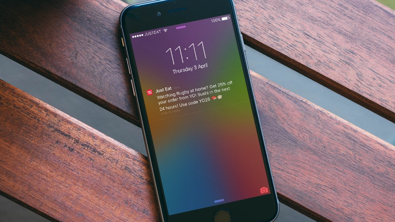 iPhone on wooden surface showing Just Eat notification with a 25% off sushi offer and code YO25.
