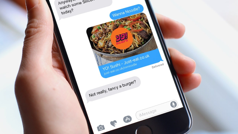 Close-up of hand holding phone showing a text conversation about food with a noodle bowl image link.