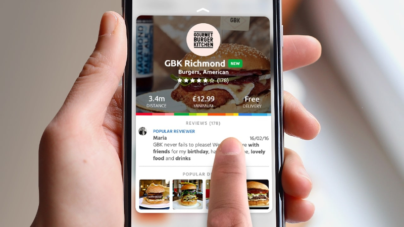 Hand holding phone showing Gourmet Burger Kitchen Richmond with ratings, price, and user review.