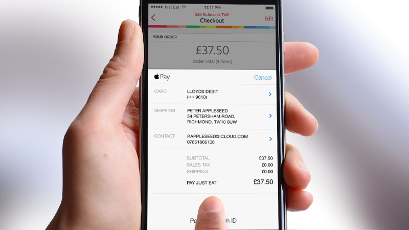Hand holding smartphone displaying Apple Pay checkout screen with £37.50 total for Just Eat order.