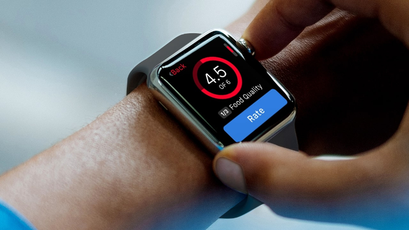 Person adjusting Apple Watch displaying a food quality rating of 4.5 out of 6 with a Rate button.