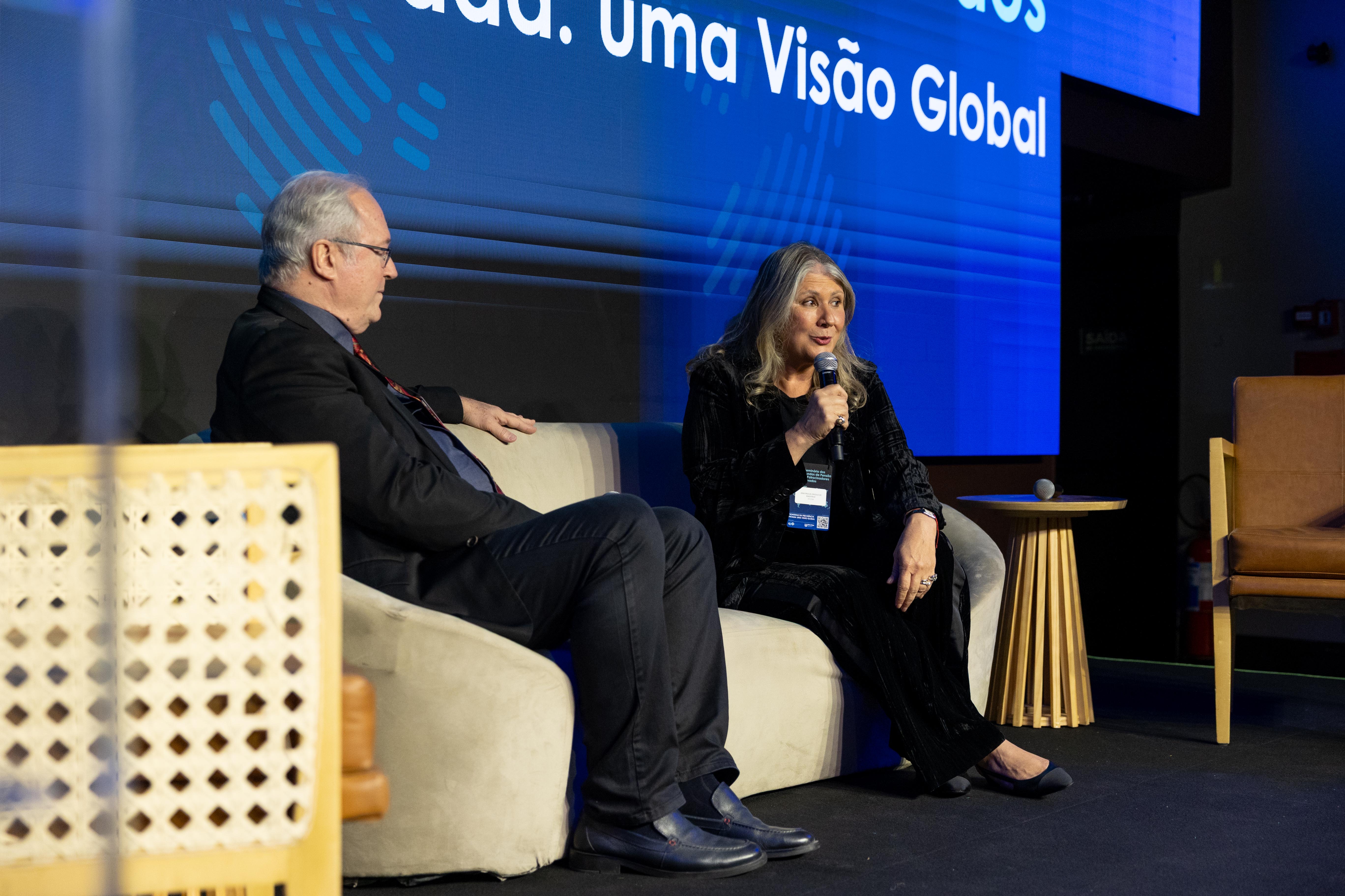 Palestrante em um seminário apresenta uma apresentação de investimentos em um palco com telões, incluindo o tema “Oportunidades no Mercado Internacional”, durante o 5º Seminário de Fundos de Pensão e Patrocinadores Privados.