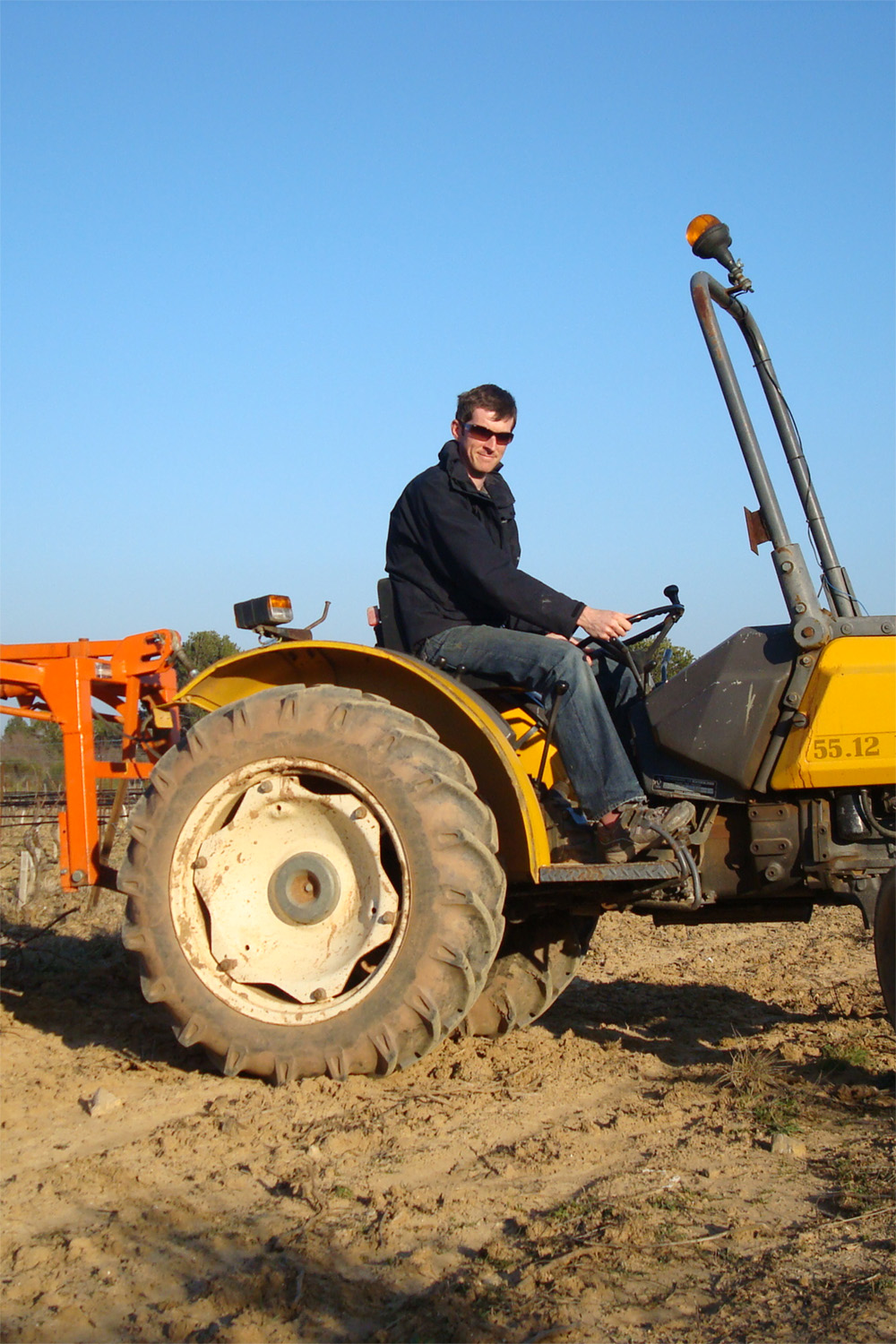man driving a yellow tractor through a bare field
