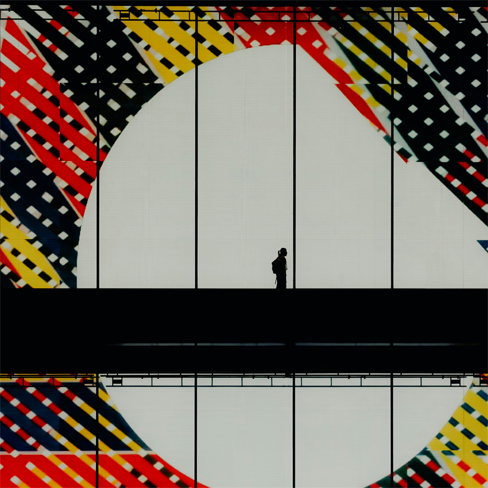 Silhouette of person walking across a high walkway in front of giant red black and yellow striped artwork