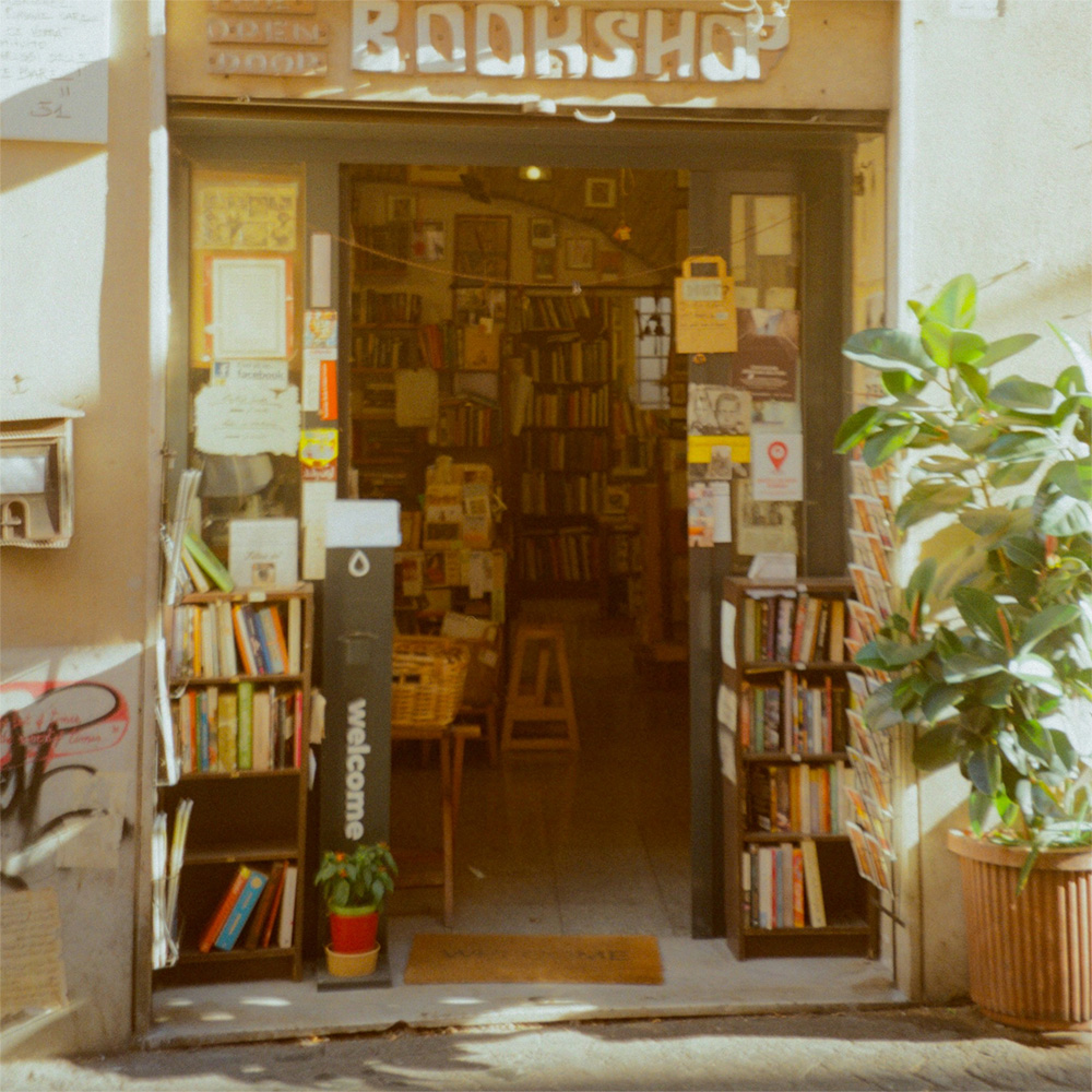 The entrance to a bookshop with plants and sunshine casting shadows on the pavement
