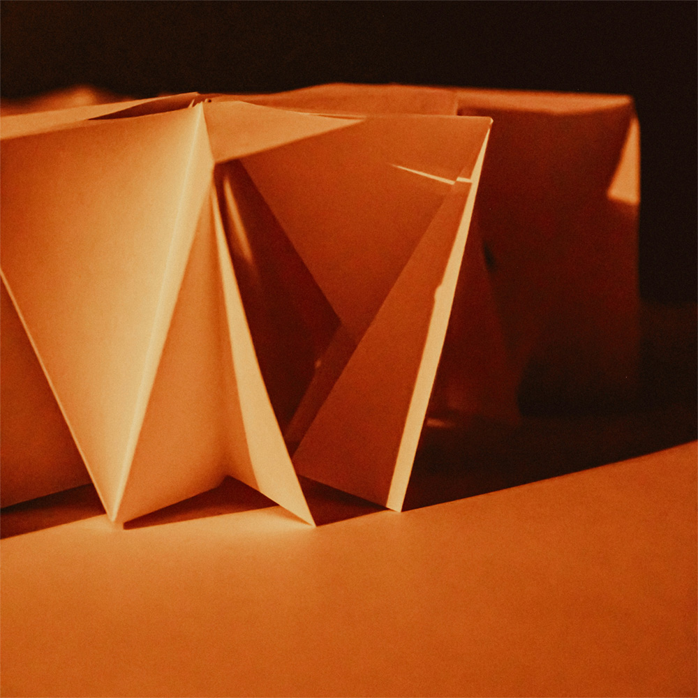 Orange paper origami shape with light and shadow on the folds, placed on orange table top