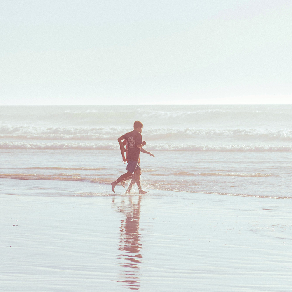 Men running on the beach towards the sea with waves breaking on the shore