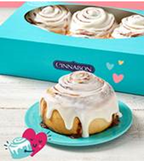 a blue cinnabon box with three cinnamon buns and on a robinegg blue plate is a cinnamon bun with a heart graphic