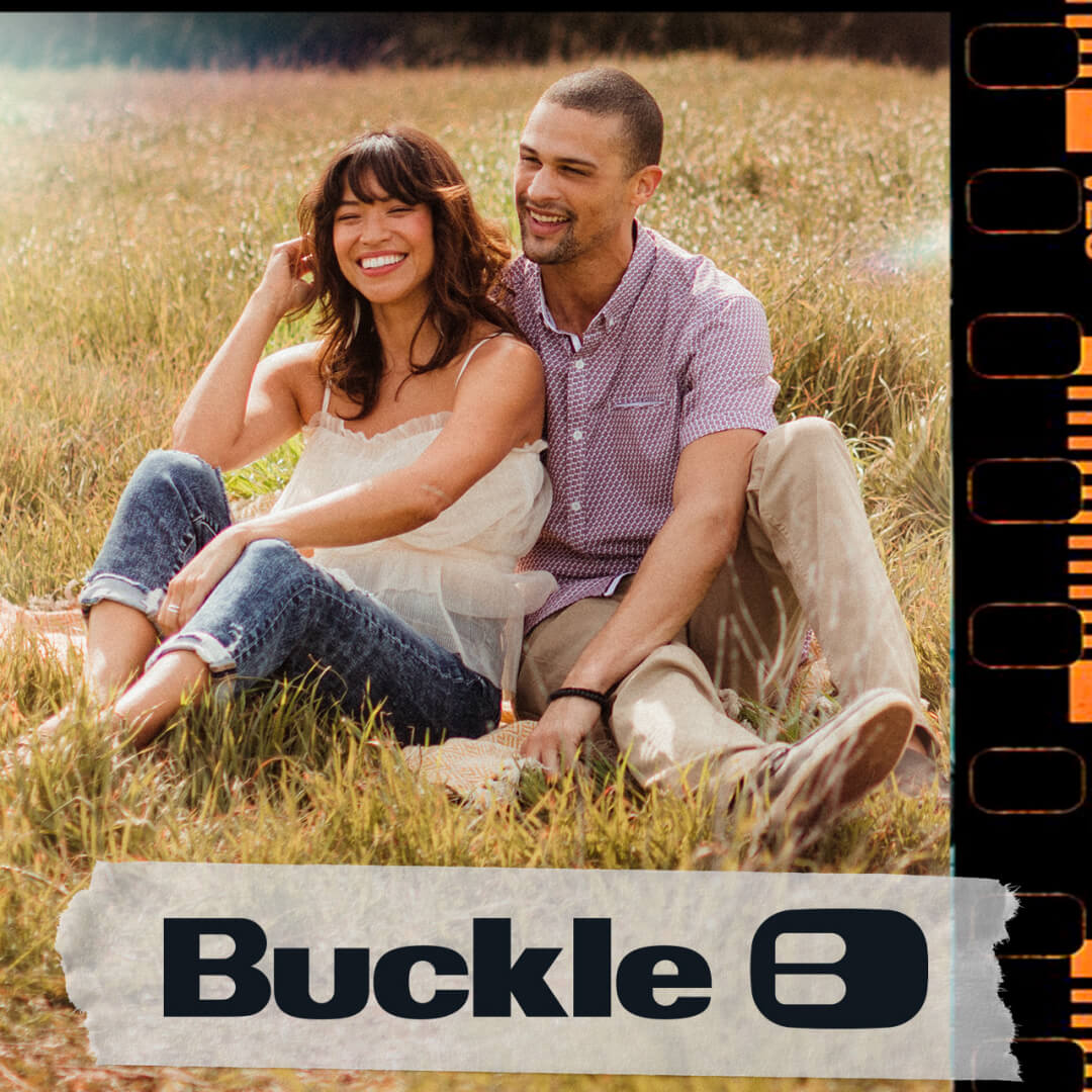 Couple sitting in a field wearing Buckle apparel