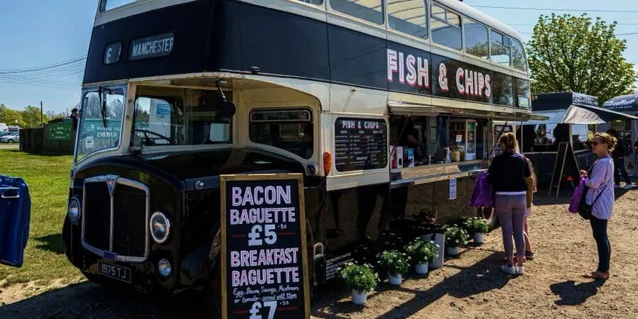 Vintage double-decker bus converted into a fish and chips food stall with customers and menu boards outside.