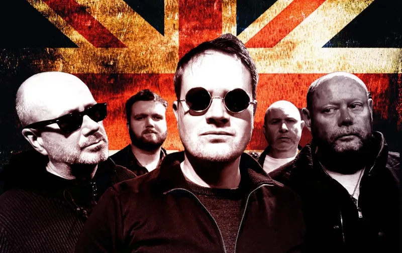 Five men with serious expressions standing in front of a Union Jack flag background, one man wearing round sunglasses at center.