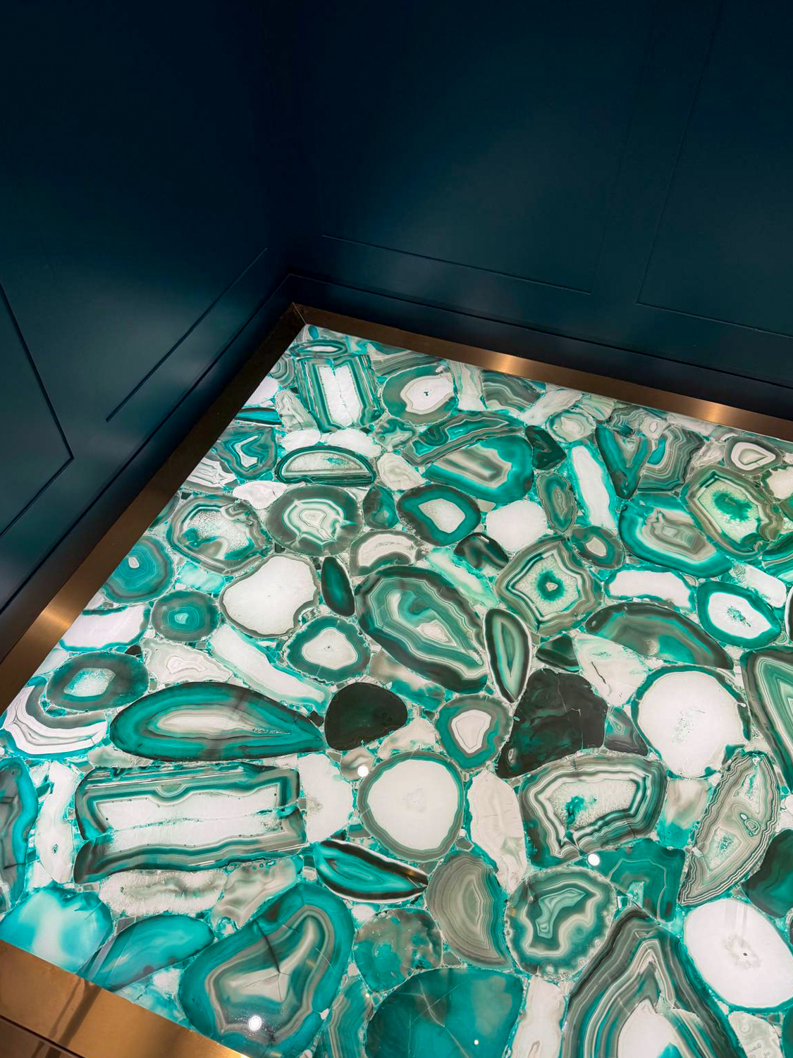 Backlit floor panel made of polished green and white agate stone slices with a metal frame.