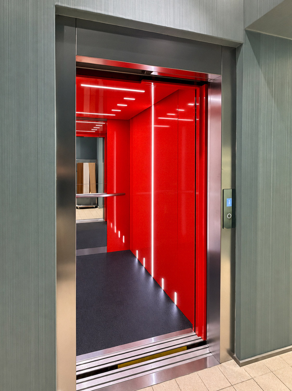 Open DDA-compliant public retail lift with bright red interior walls, black floor, vertical and horizontal white LED strip lights, and stainless steel frame with floor indicator showing 1.