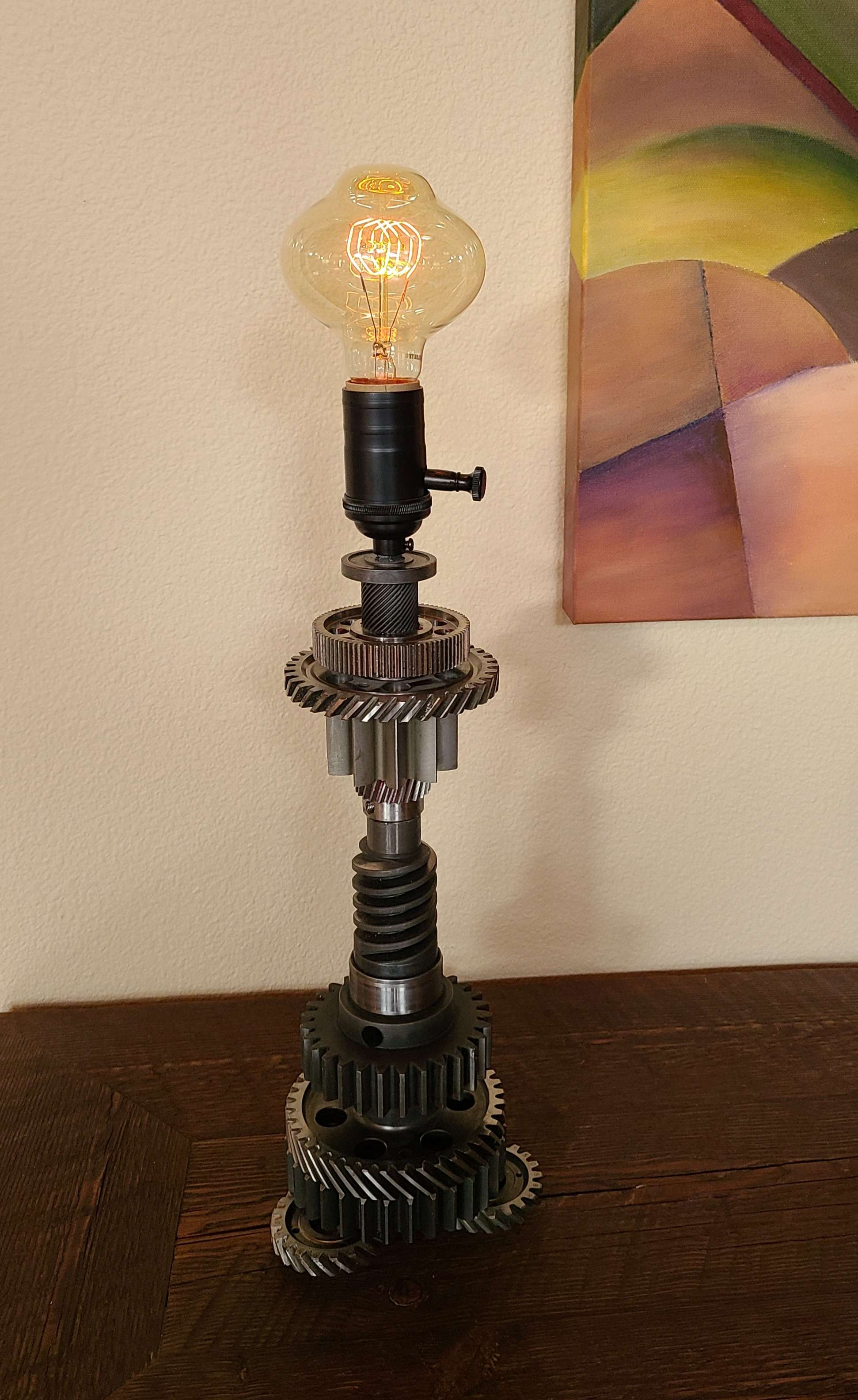 Lamp made of misc. vintage gears, with built-in dimmer switch and 40 W Edison loop bulb. 16" high without bulb. 42" grey twisted cloth plug.