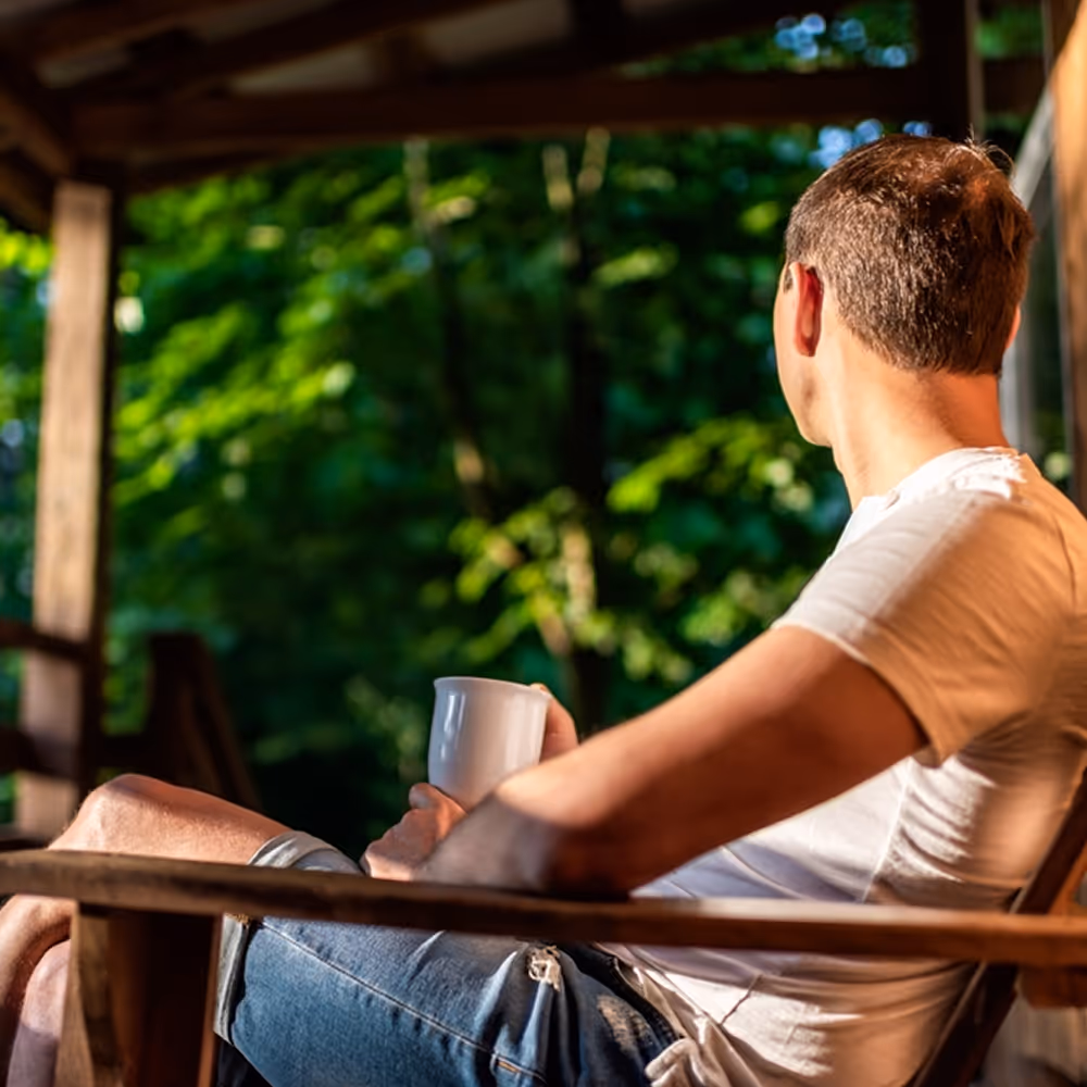A male former resident, now in outpatient recovery, enjoying a coffee on his porch at sunrise.
