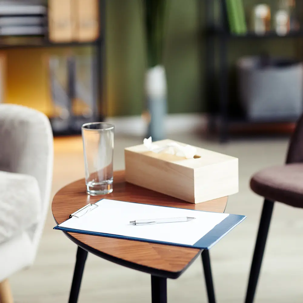 A clipboard, glass of water, and box of tissues on a table in a therapy room, symbolising the supportive and professional environment at The Hader Clinic for addiction and mental health treatment.