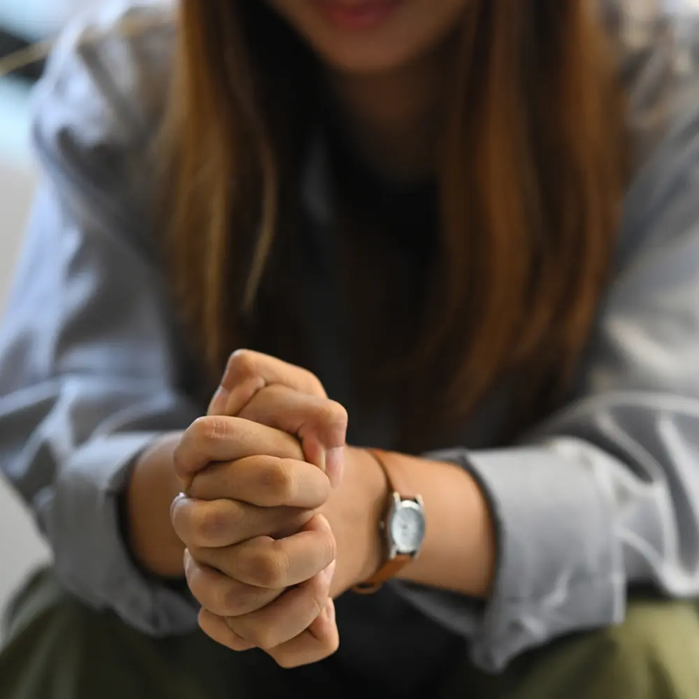 A woman sits alone on a sofa with her hands clasped, reflecting on the emotional challenges of addiction and the need for compassionate drug treatment programs.