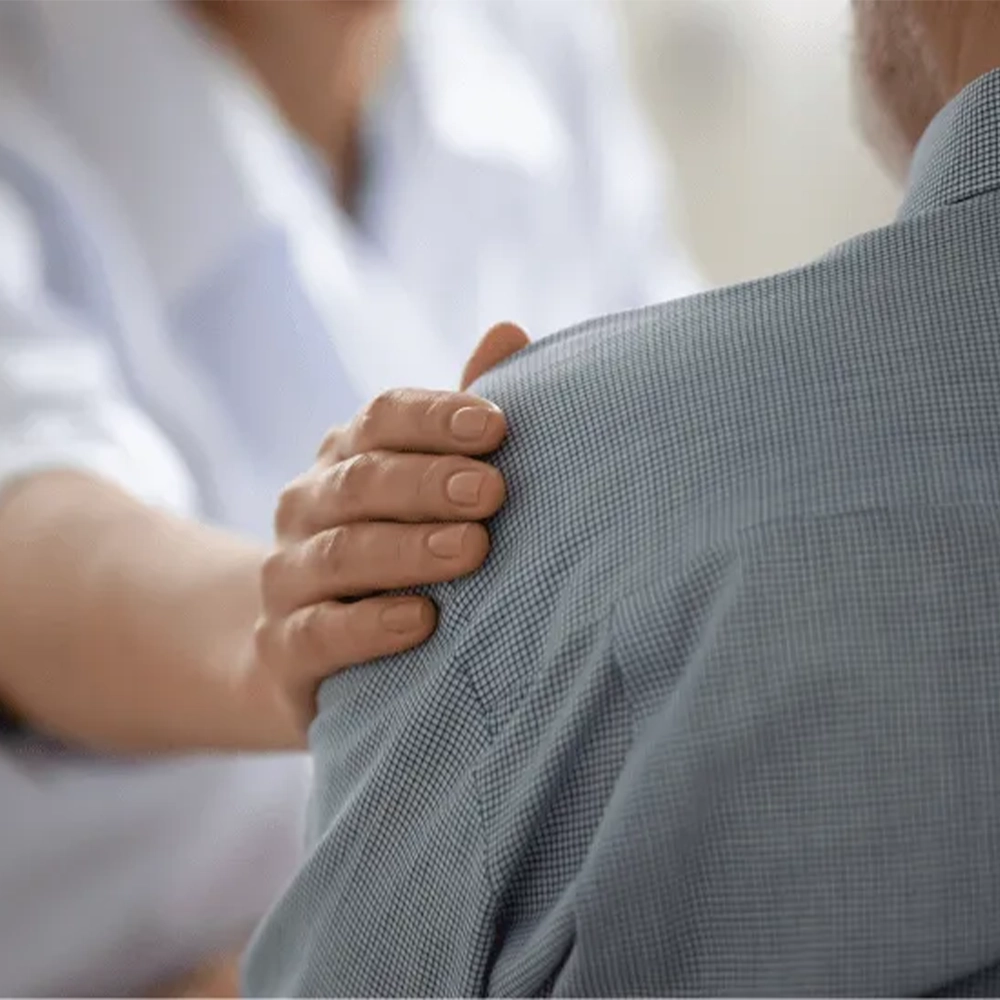 Caregiver offering comfort and support by placing a hand on a person’s shoulder.