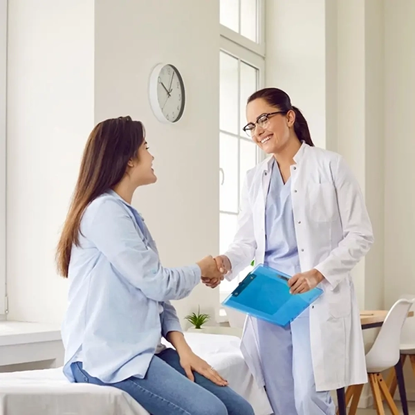 Smiling doctor shaking hands with a patient during a consultation in a bright medical office.