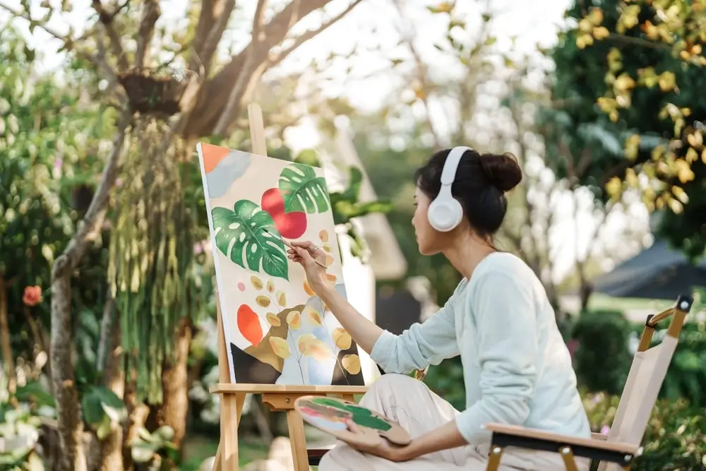 A resident sitting in the garden and painting floral art to calm herself. She’s got headphones to block out distractions. Mindfulness can help people overcome cravings during rehab detox.