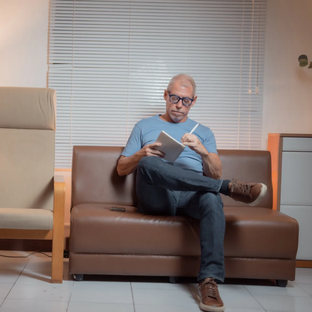 A resident sitting on a couch in a shared space, working on his personal journal as part of his court-ordered rehabilitation.