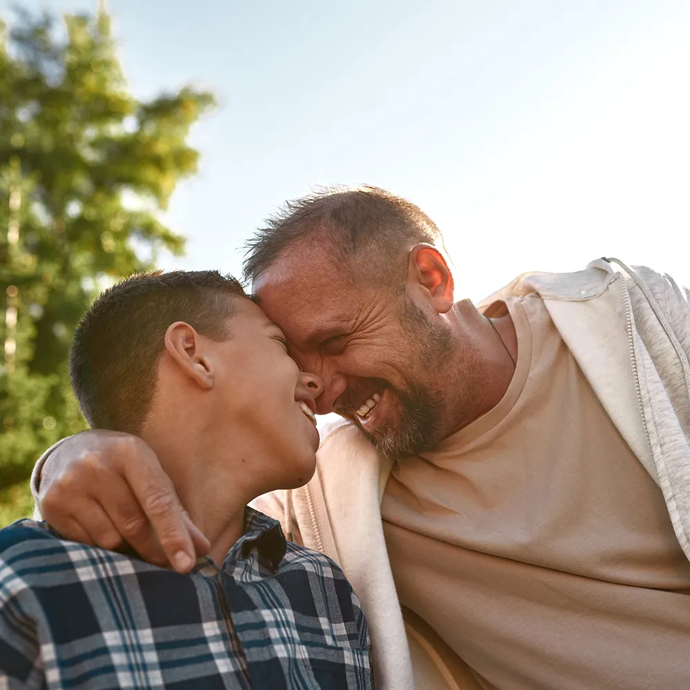 Father and teenage son sitting head to head on a park bench, sharing a quiet, joyful moment and strengthening their bond during recovery