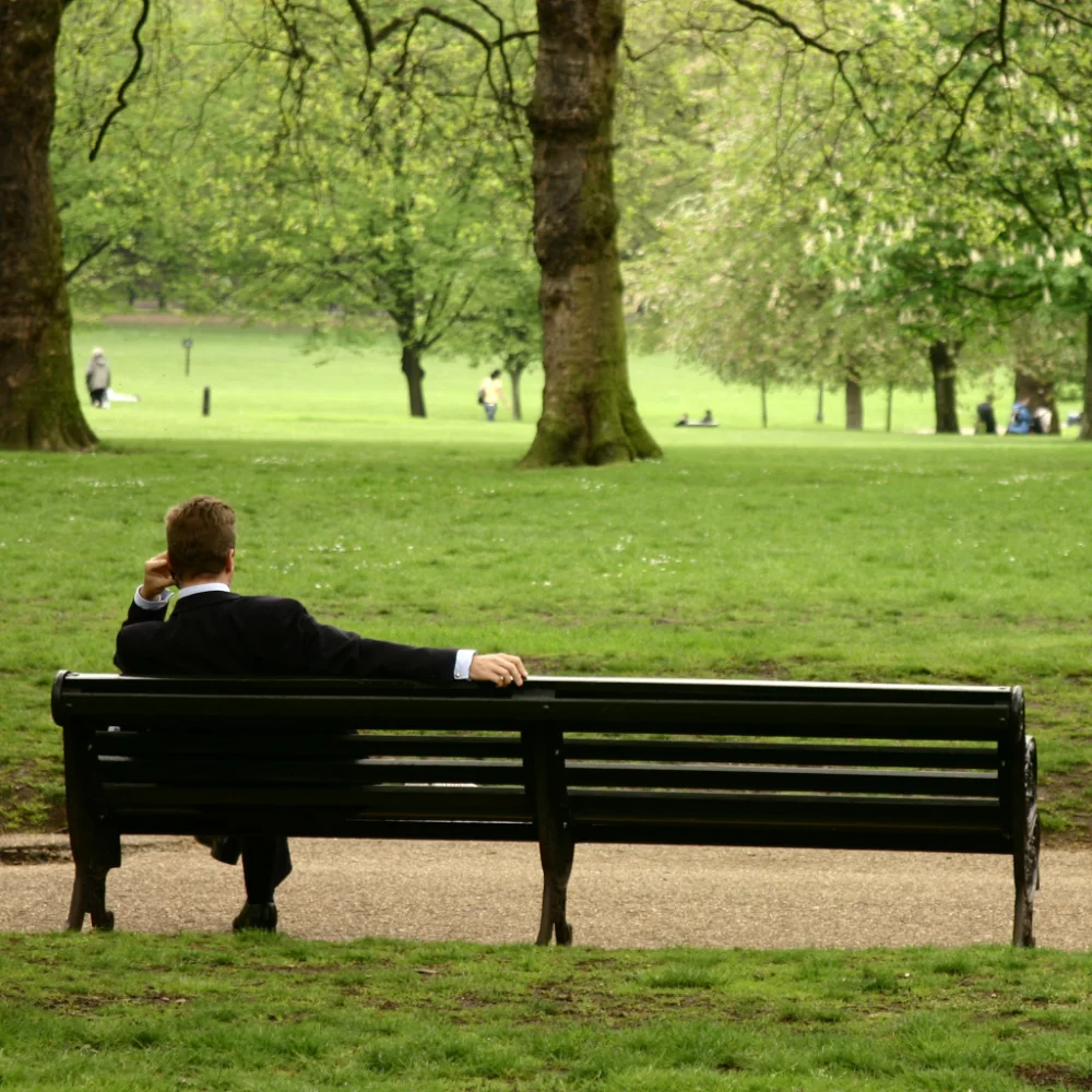 Man sitting in a Melbourne park attending an online therapy session on his phone as part of the Hader at Home digital rehab program