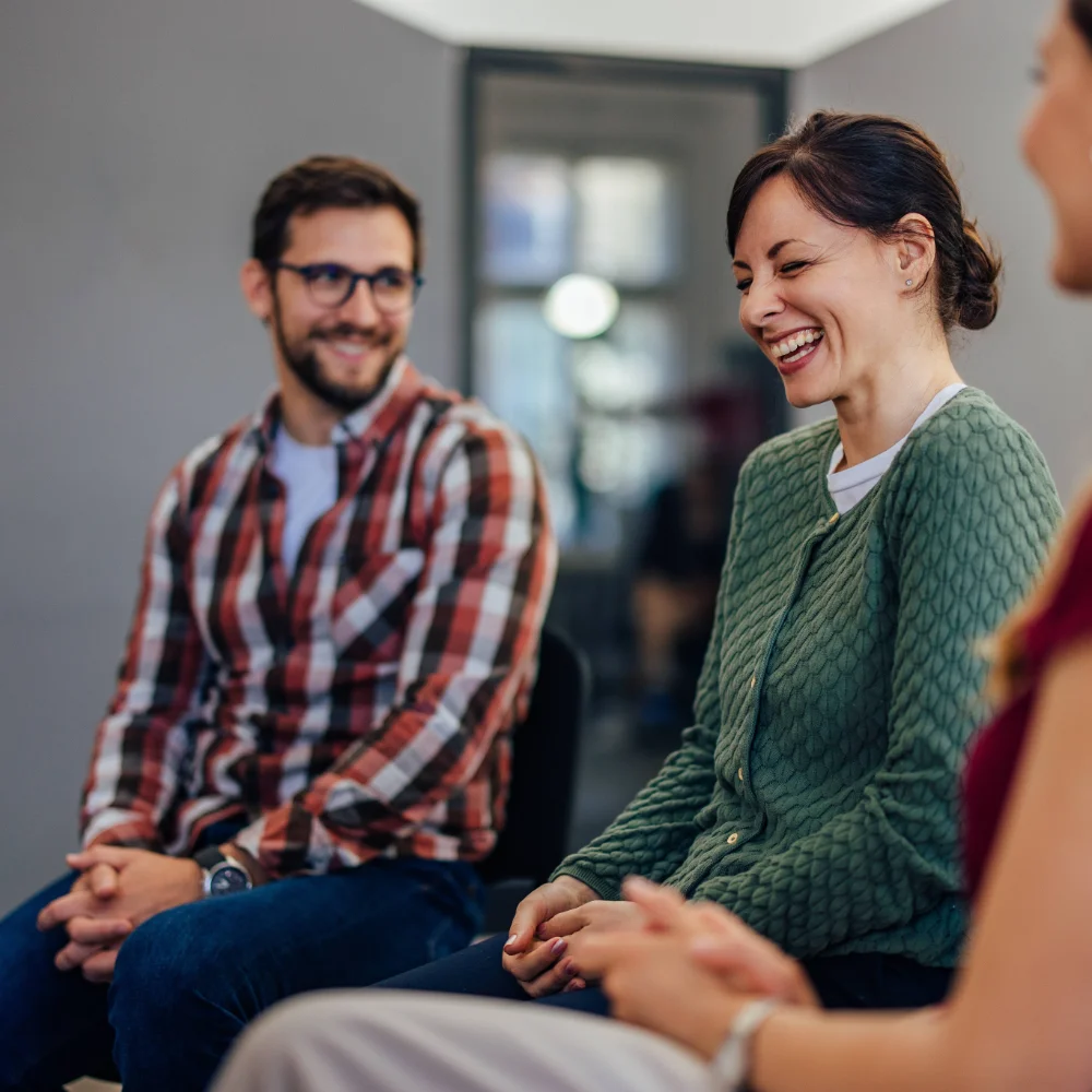 Brunette woman smiling and sharing a personal breakthrough during group therapy, celebrating progress in her outpatient recovery journey.