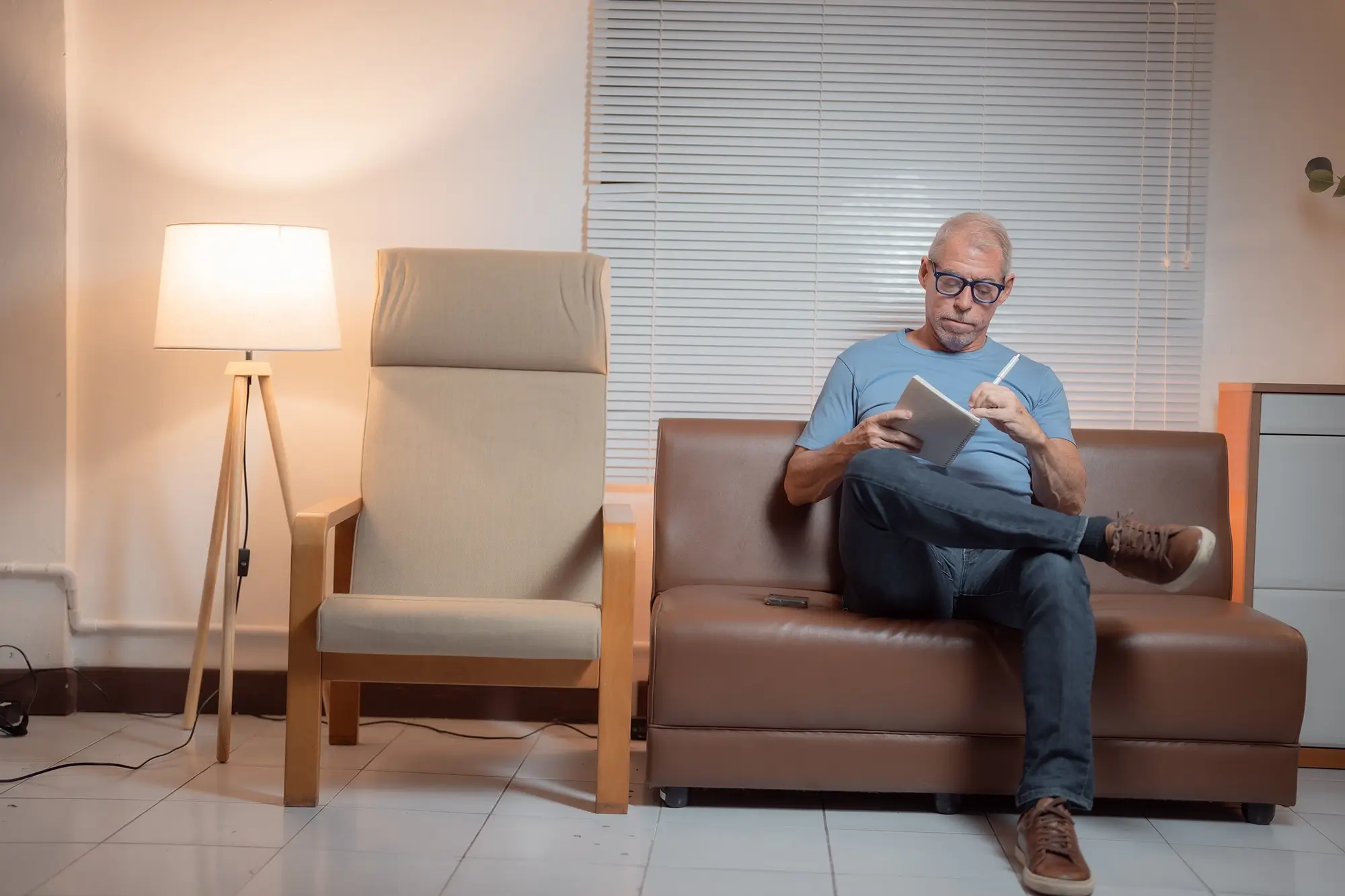 A resident sitting on a couch in a shared space, working on his personal journal on his rehab counsellor’s advice.
