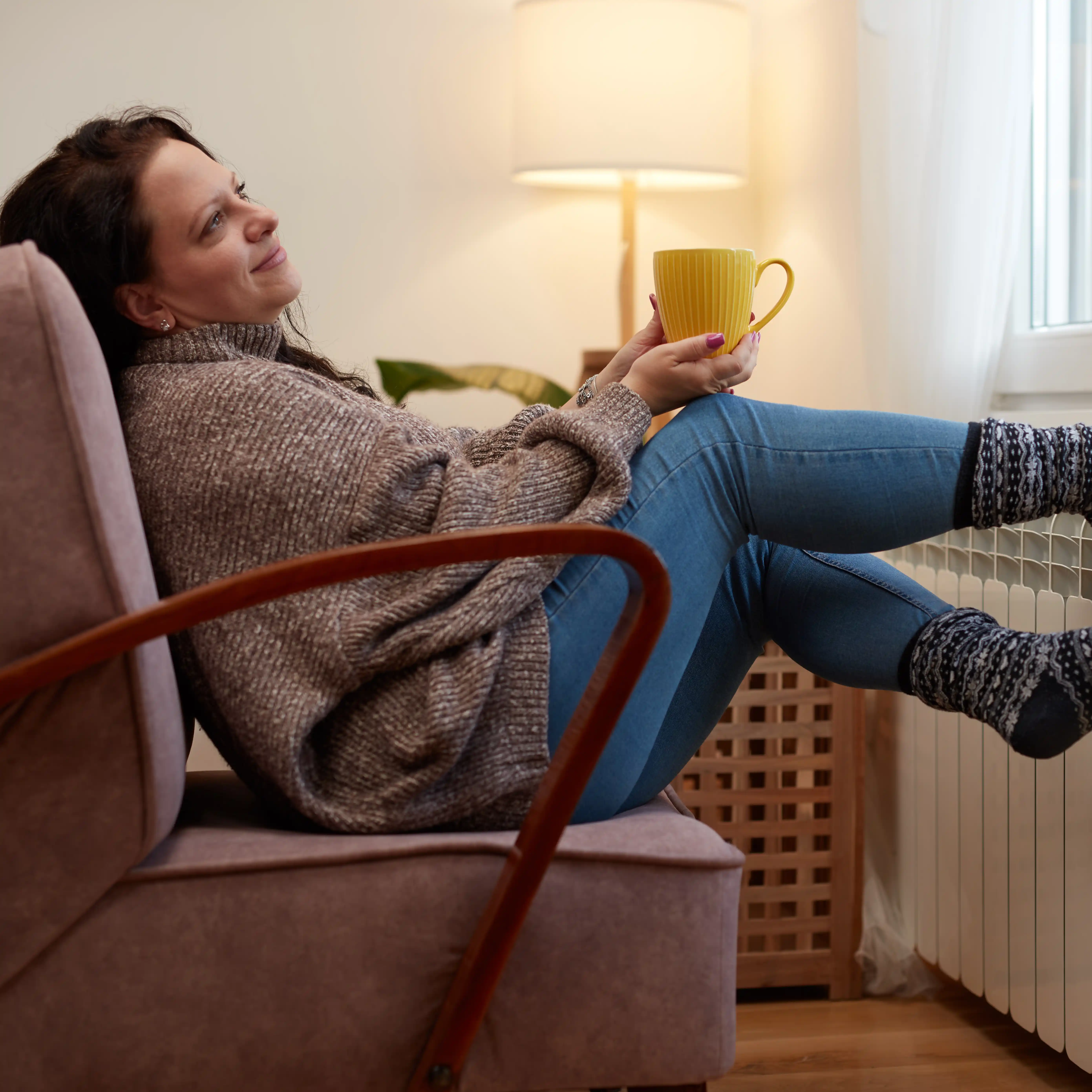 A woman sits curled up on a chair, warming her feet with a blanket in a chilly room — symbolising the physical and emotional vulnerability that can accompany ecstasy addiction and the need for a supportive ecstasy rehab environment to foster warmth, safety, and healing.