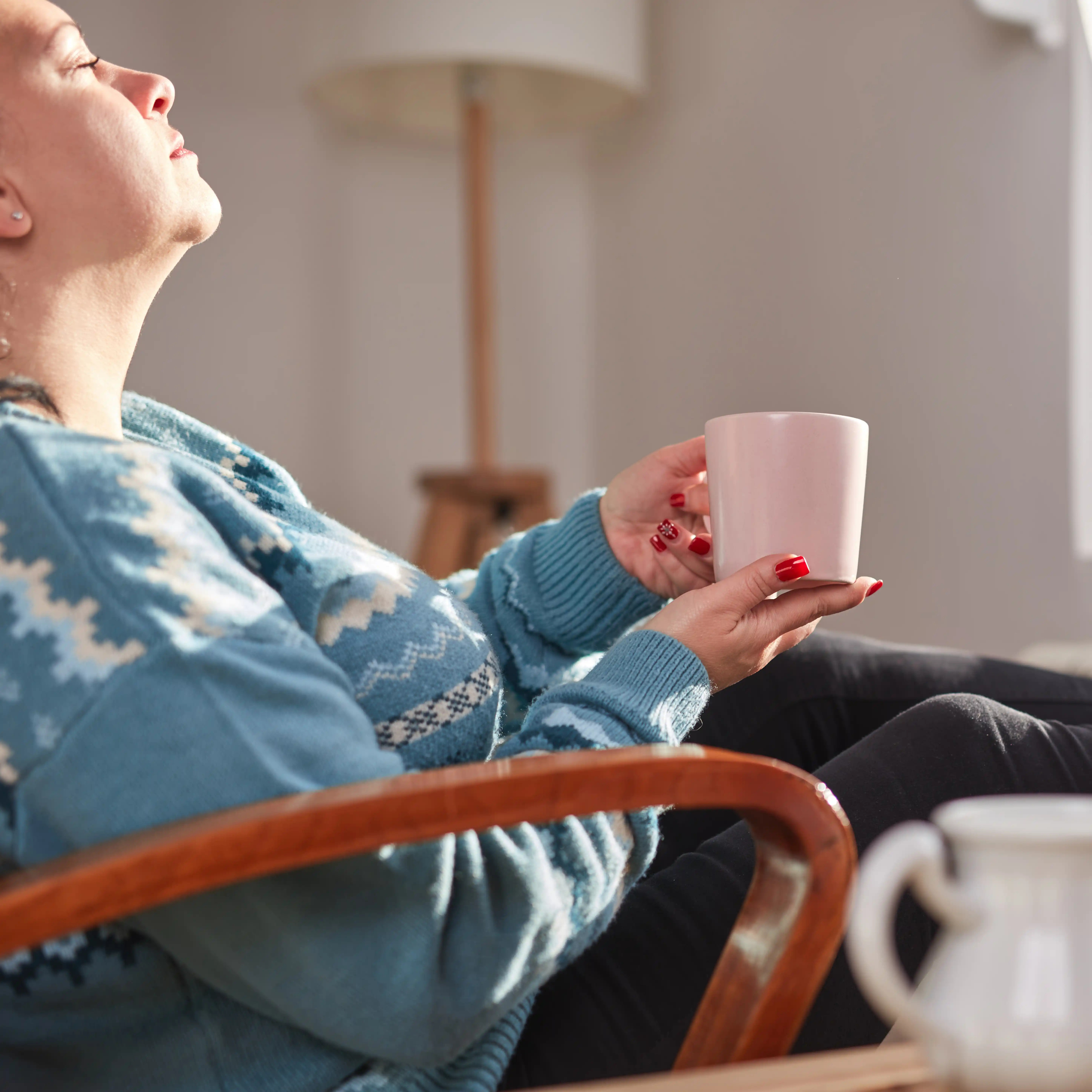 A woman sits in her personal dorm at a rehab centre, drinking tea and warming herself by the radiator, reflecting the quiet, restorative moments that are part of the healing process in heroin rehab.