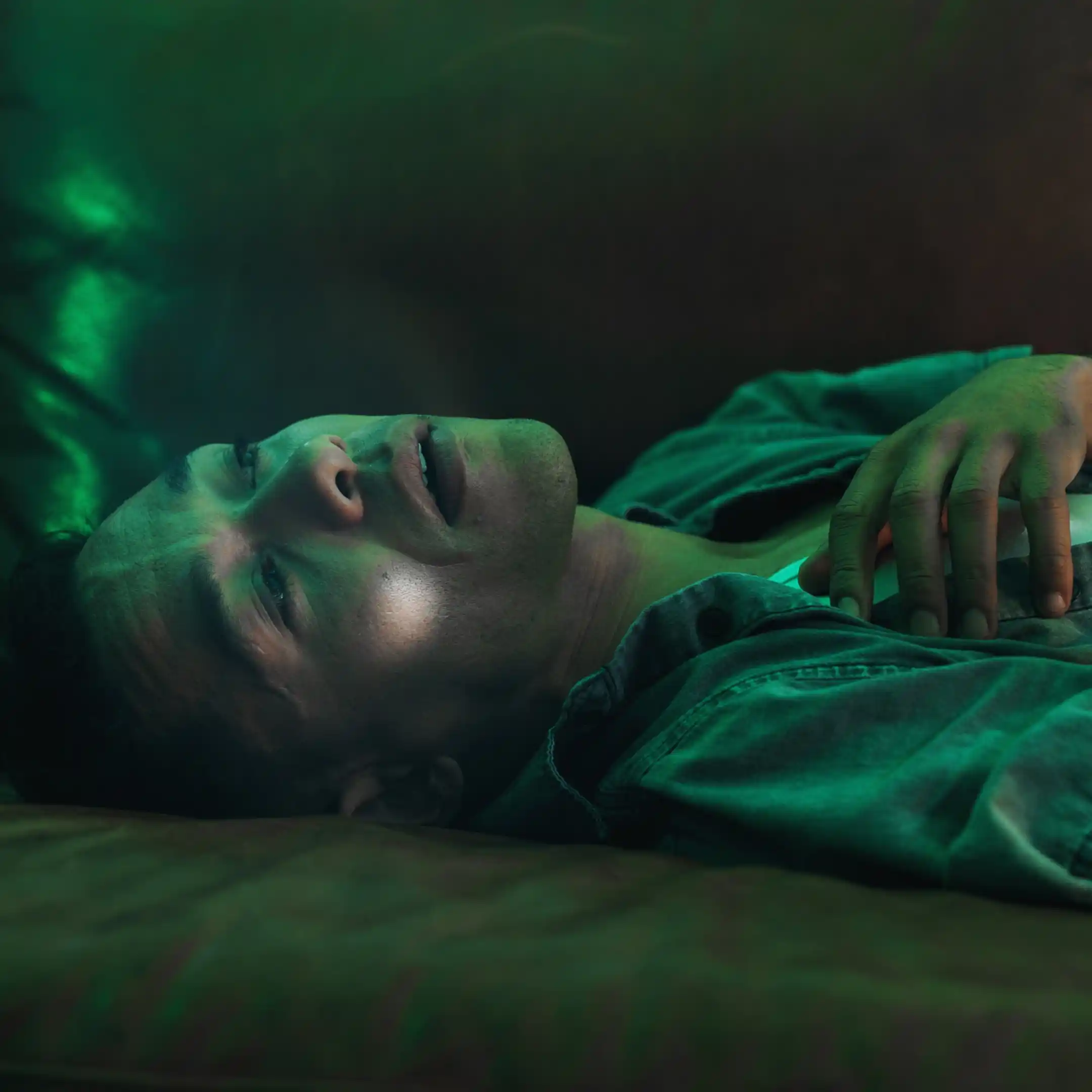 A man lies unresponsive on a couch in a dimly lit room, highlighting the serious risks of substance misuse, including the potential dangers of marijuana addiction when combined with other drugs.