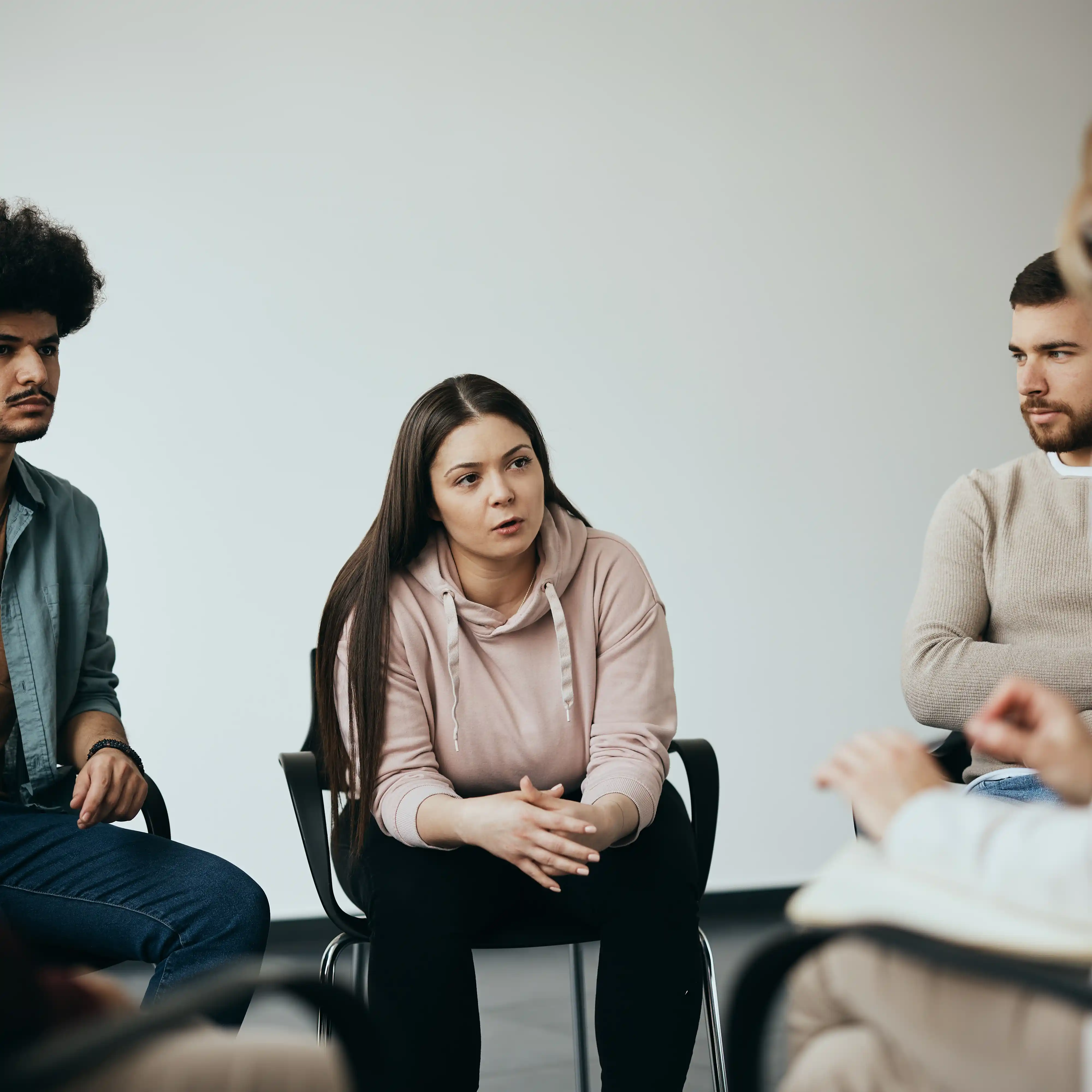 A young woman speaks openly during a group therapy session at a community centre, with a therapist and other participants listening supportively. The image reflects the importance of connection and peer support in a structured meth rehab program.