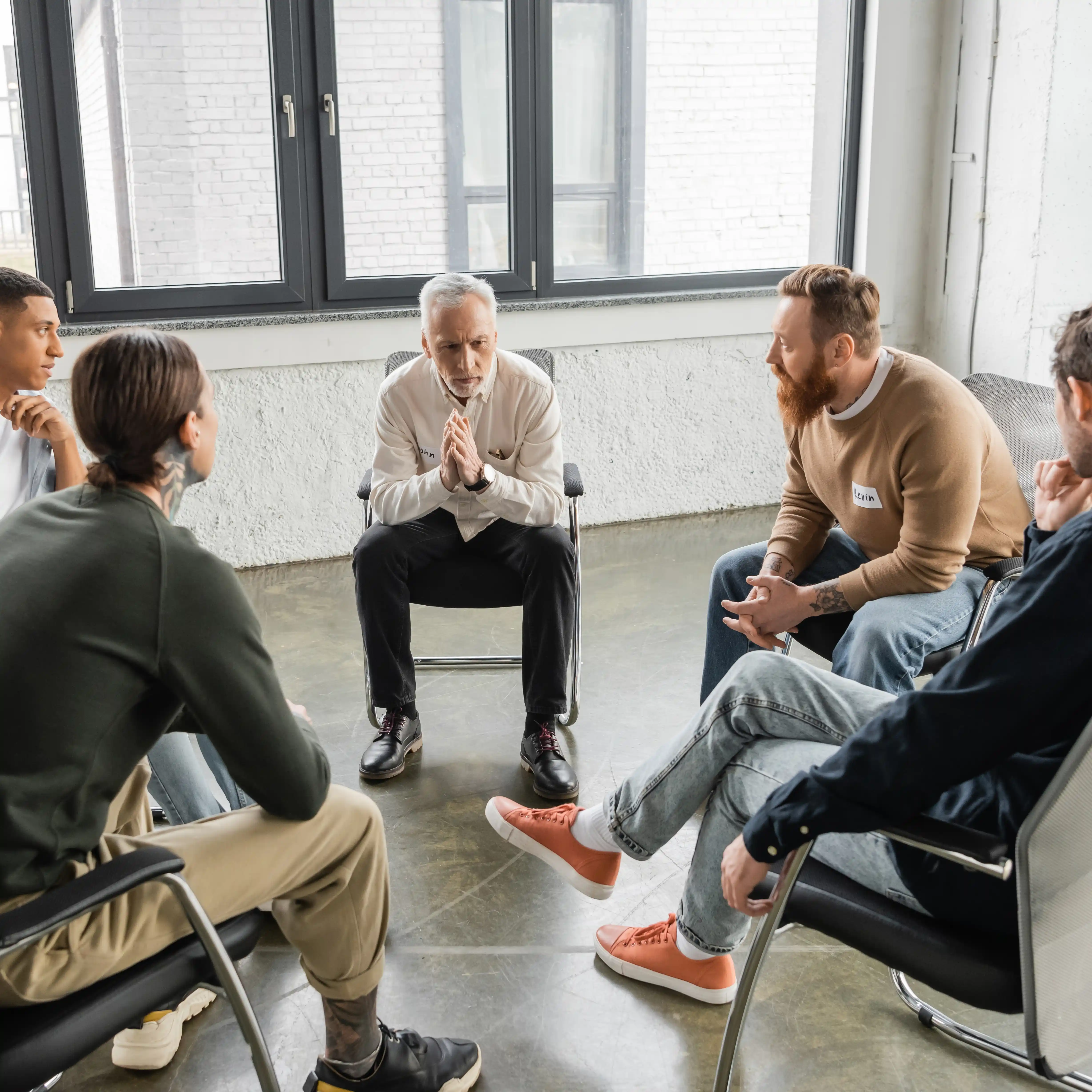 A diverse group of people sits in a supportive circle during a group therapy session at a codeine rehab centre, engaged in conversation. 