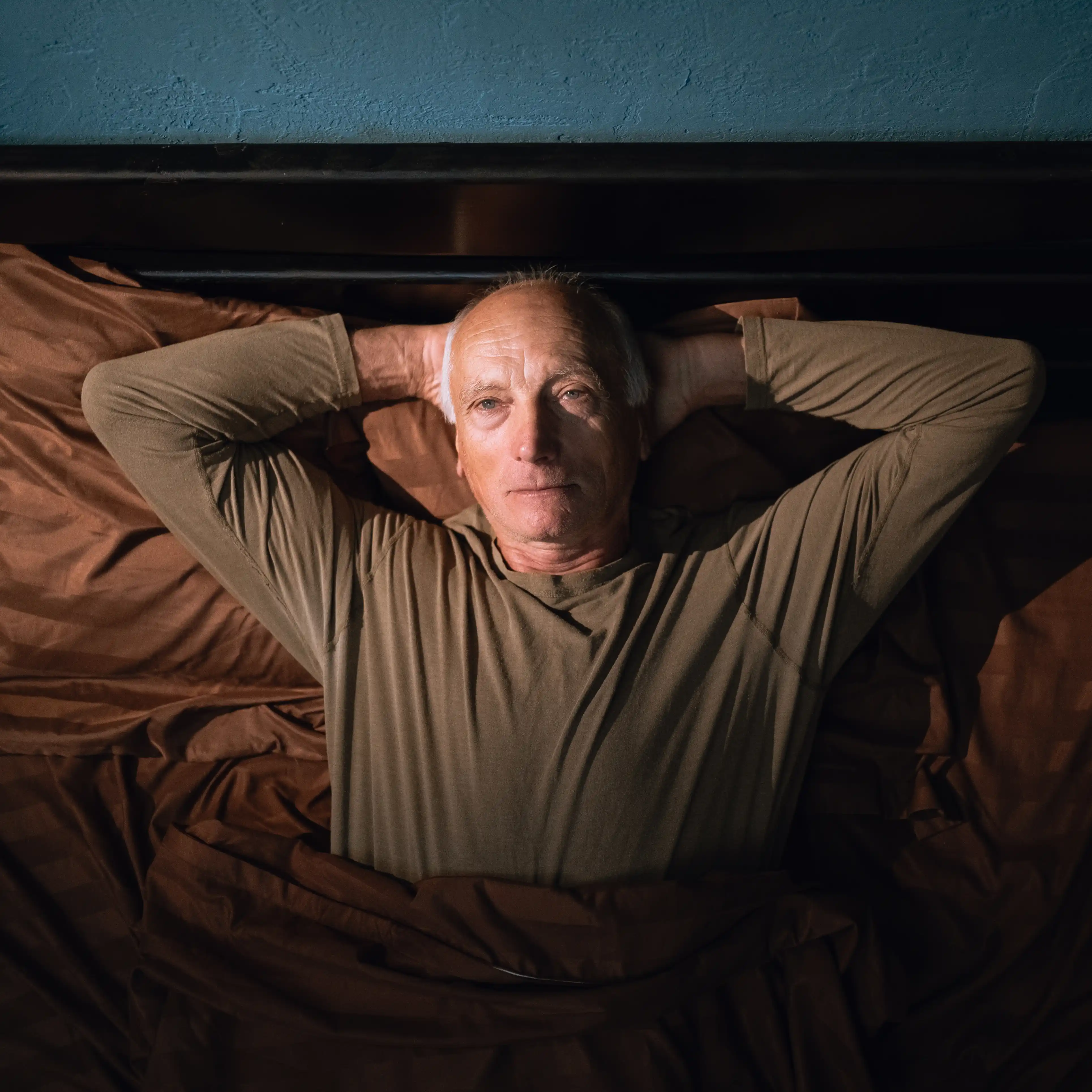 An older man lies awake in bed at night, viewed from above. The image captures the deep fatigue and emotional shutdown that often accompany long-term substance dependence, reflecting the need for compassionate codeine rehab.