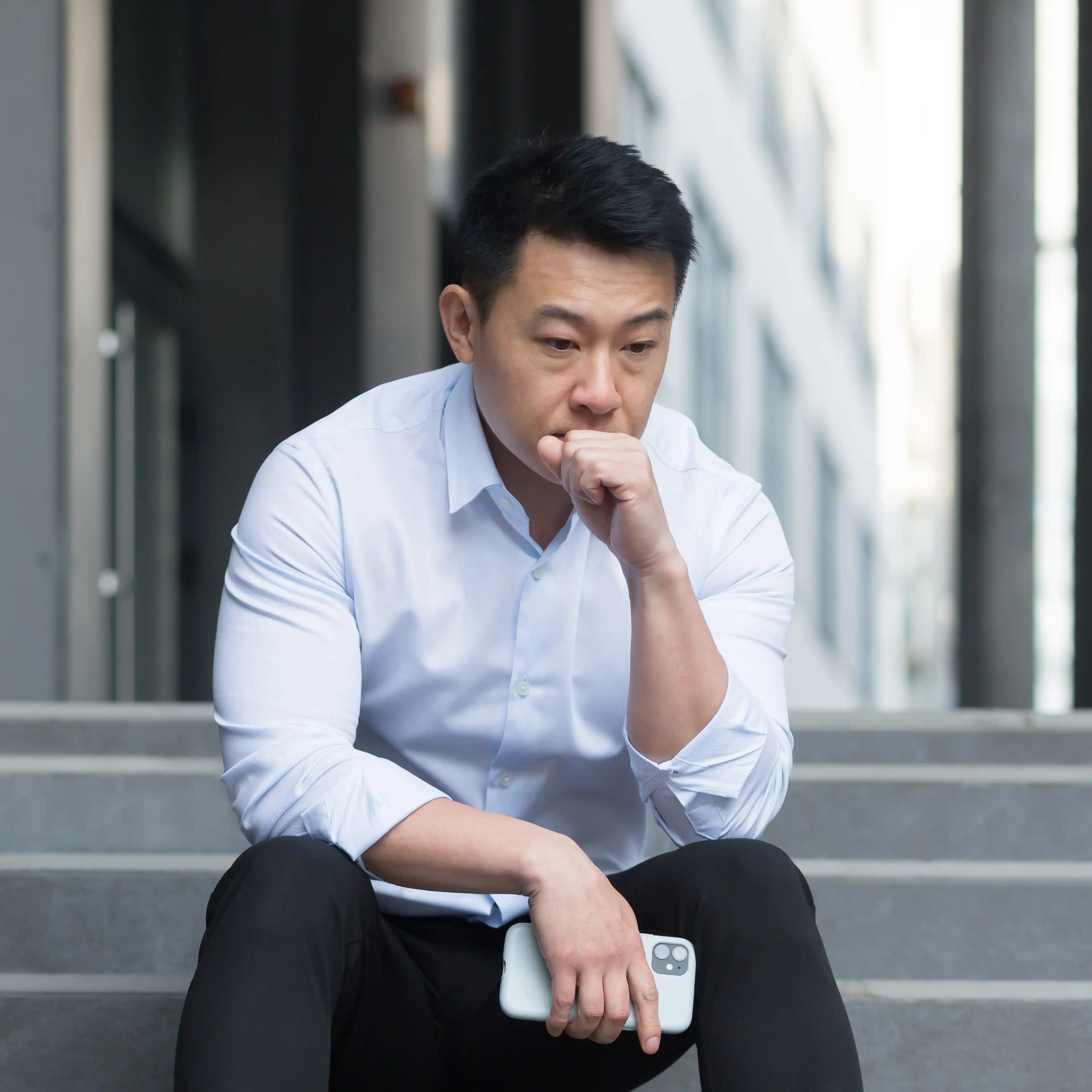  young man sits alone on outdoor steps near an office building, hunched over with his head down in visible distress. The image reflects the emotional crash and burnout that can follow compulsive reward-seeking behaviours, highlighting the need for structured recovery in a dopamine addiction rehab program.