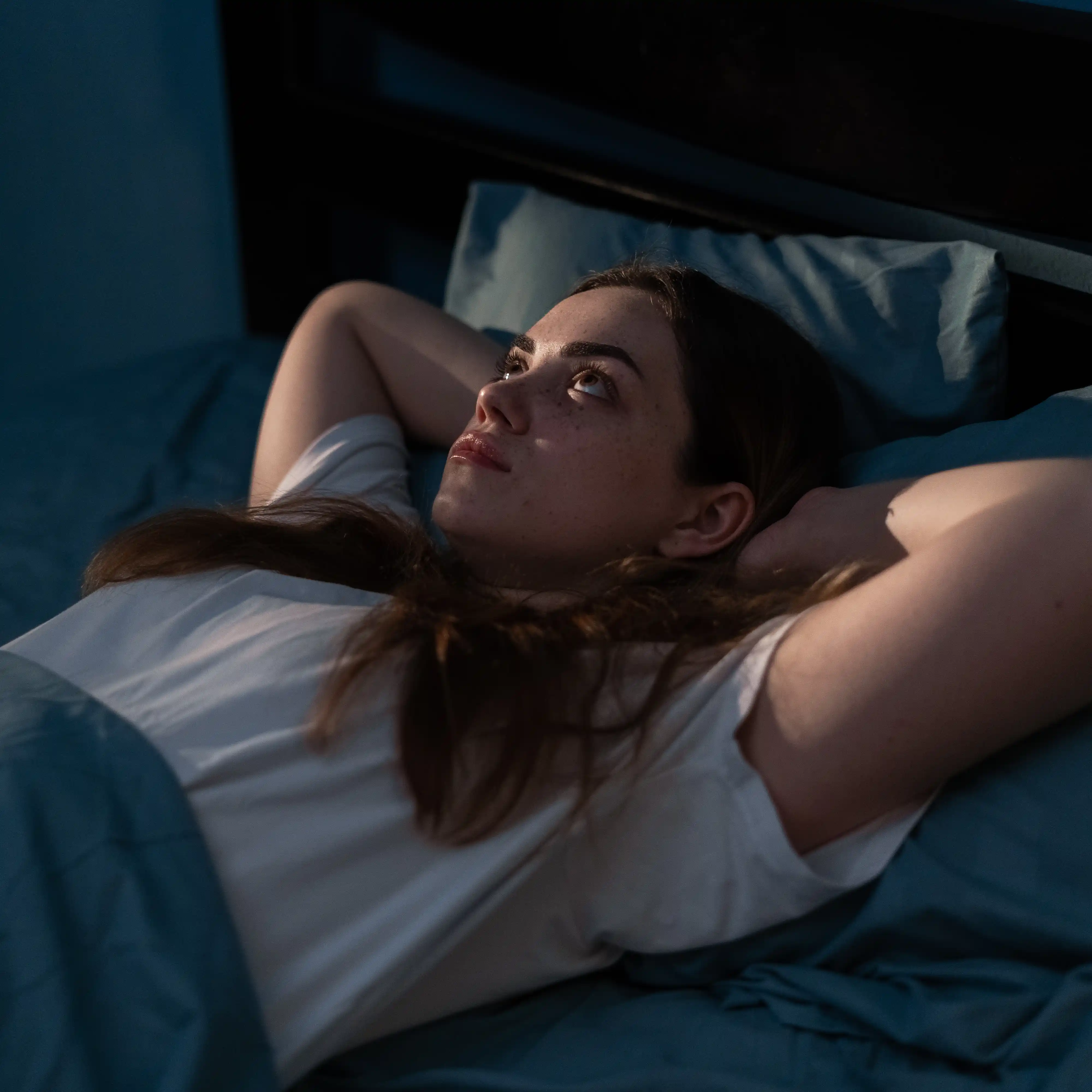 A young woman lies in bed in the dark, eyes wide open and visibly anxious, struggling with insomnia. The scene captures the sleep disturbances and emotional unrest often experienced by individuals in need of treatment at a GHB rehabilitation centre.