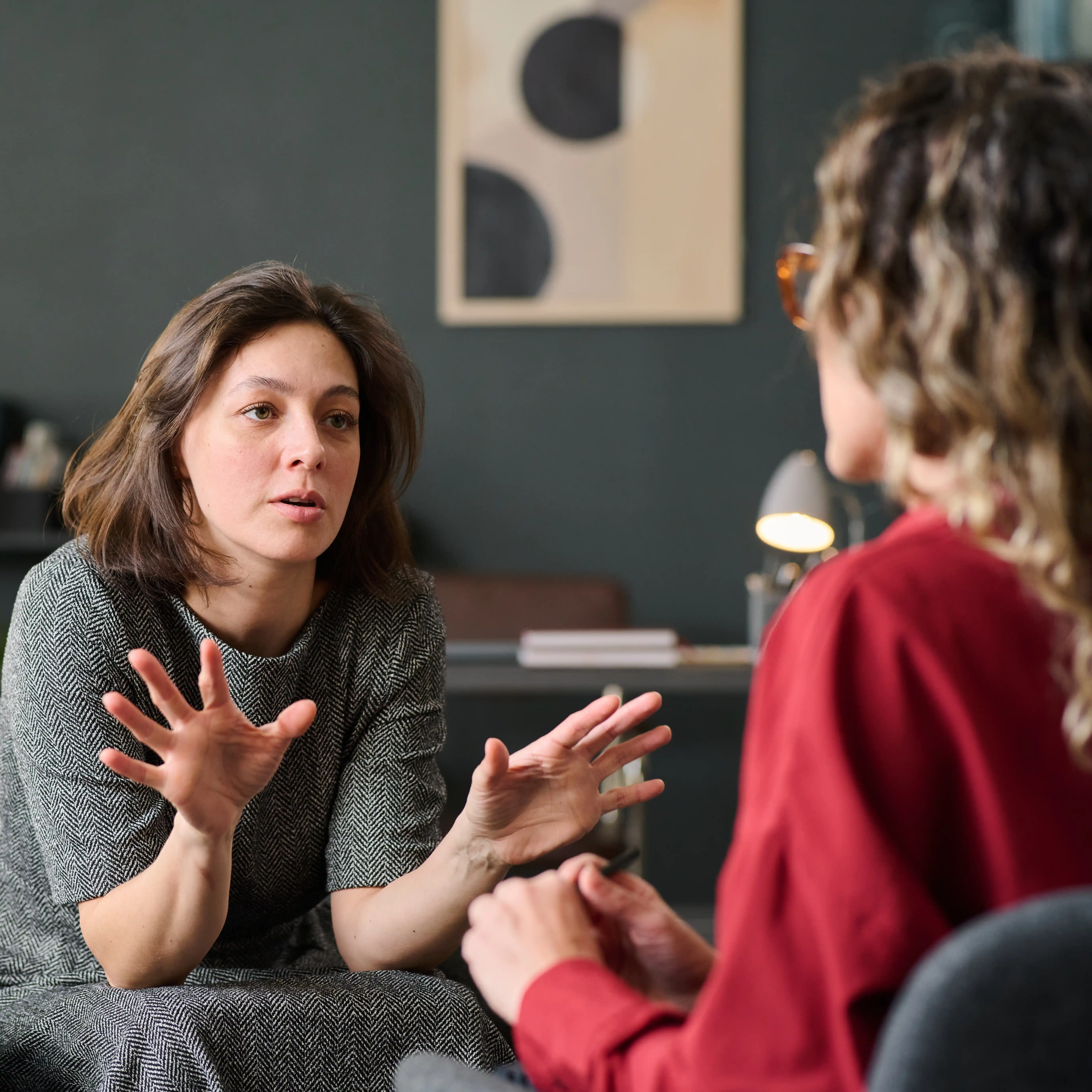 A person speaks with expressive hand gestures during a therapy session in a warm, comfortable setting, engaging in meaningful conversation. The image reflects the importance of open communication and personalised care in a GHB addiction treatment program.