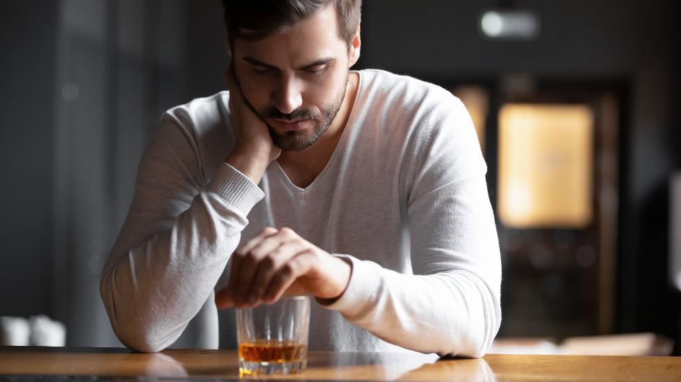 upset man sitting alone at a bar with a glass of whiskey in front of him
