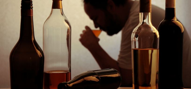 silhouette of person drinking behind bottles of alcohol