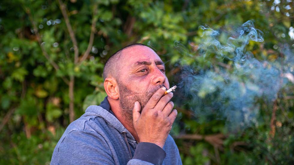 A stressed man smokes a cigarette outdoors.