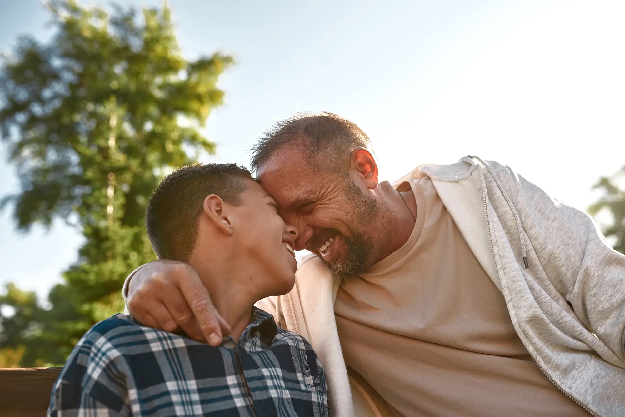 Father and teenage son sitting head to head on a park bench, sharing a quiet, joyful moment and strengthening their bond during recovery