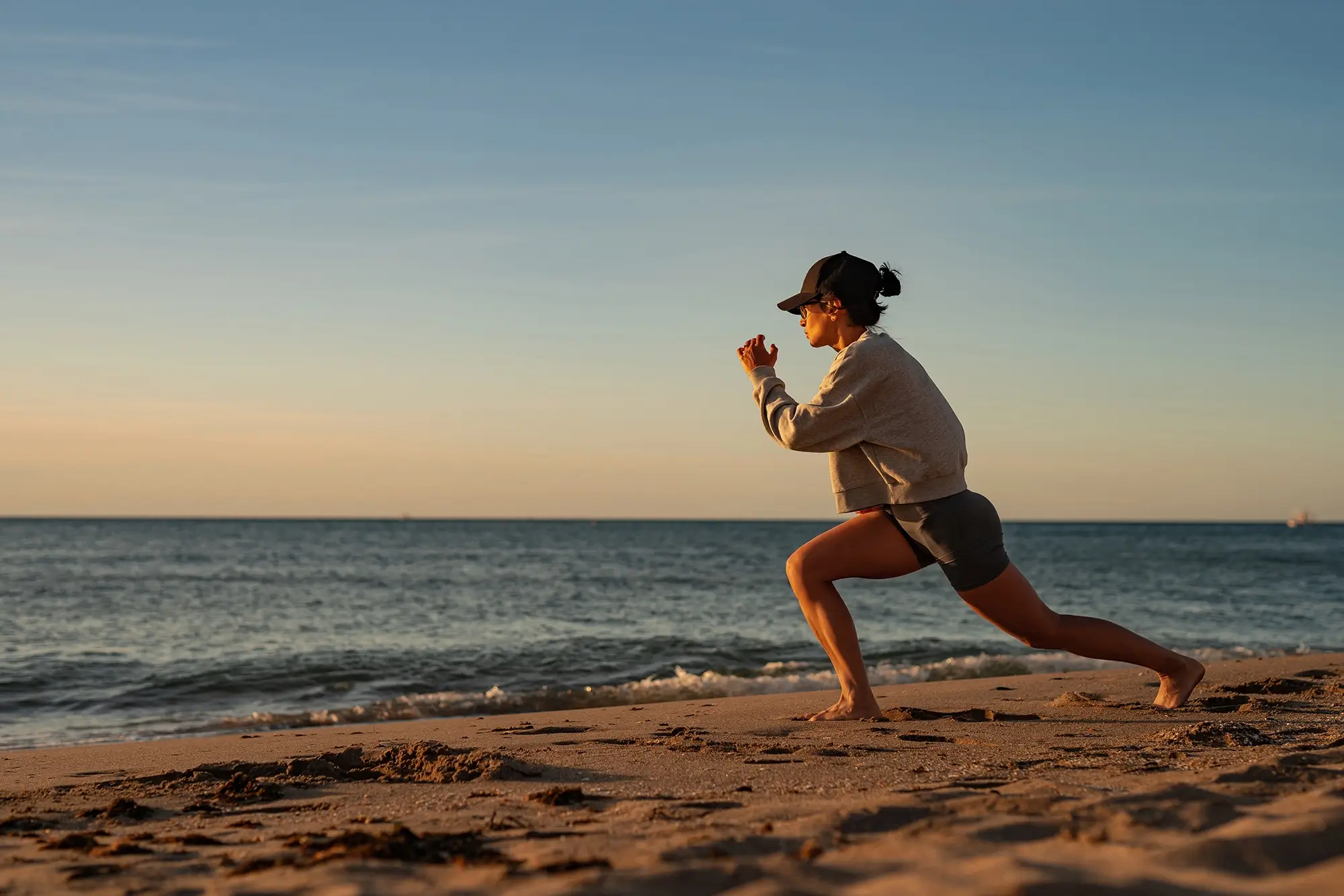 Woman practising mindful movement on the beach at sunset as part of a personalised wellness routine.