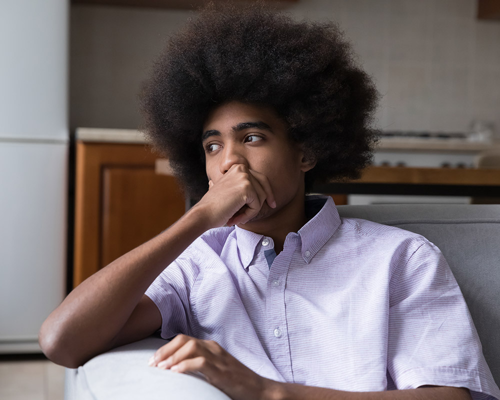 A young man looking away with sadness in his eyes, hands on his mouth.