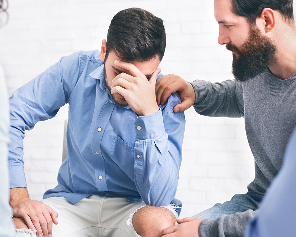 A bearded man showing concern over another patient suffering from addiction