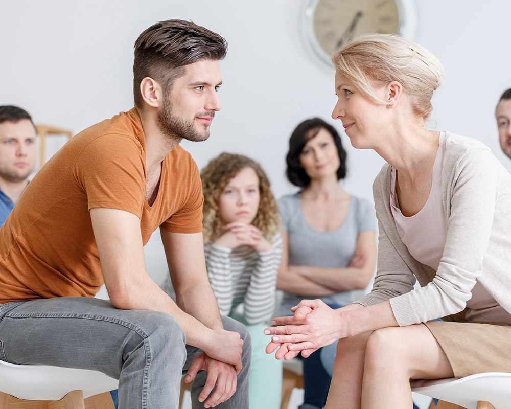 A young man and a mother smiling to each other as they undergo a family therapy session. 